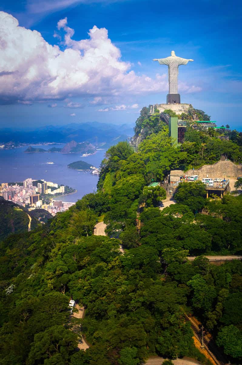 A forested peak carries Christ the Redeemer above Rio's neighborhoods, bay, and layered mountains in Rio de Janeiro, Brazil.